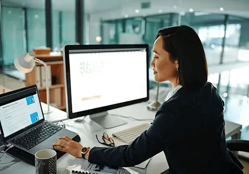 Woman working on multiple computer screens